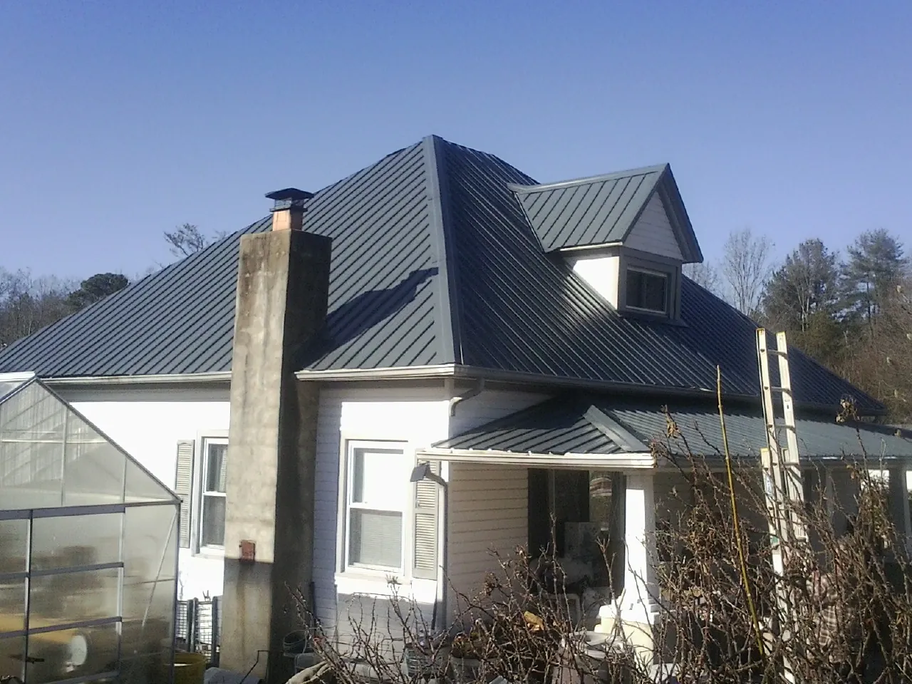 Dark blue standing seam metal roof on a white farmhouse with dormer — Slate & Tile Roof Repair by Roofing Brothers in Waller
