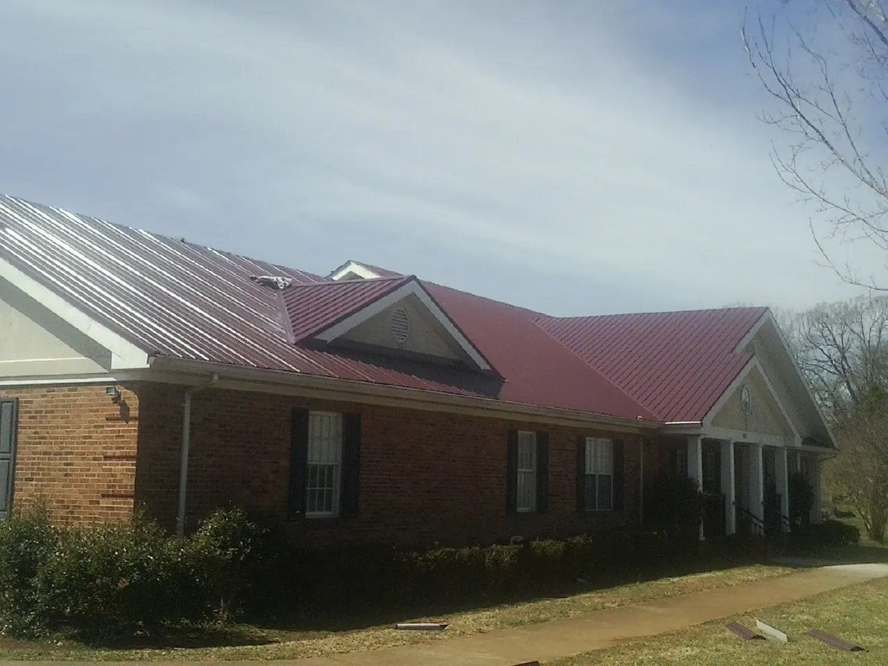 Red metal roof with gabled entries on a long brick building, from a Hail Damage Roof Repair job in Waller