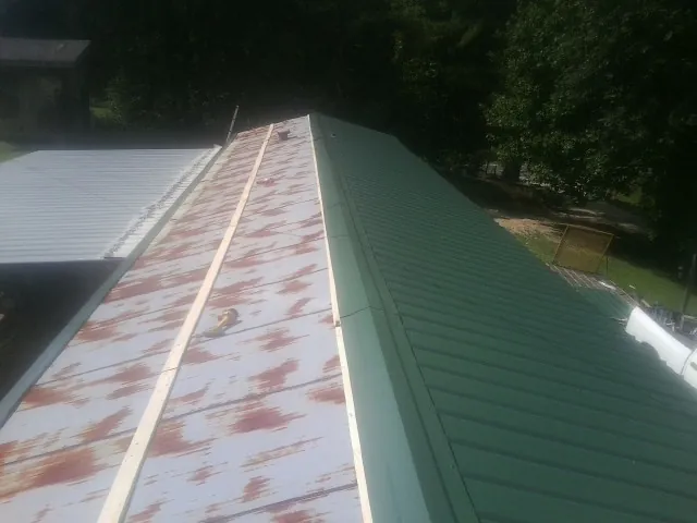 Old rusted panels beside newly installed green metal roofing — Wind Damage Roof Repair by Roofing Brothers in Waller