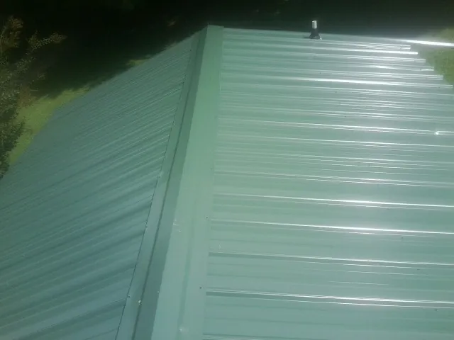 New green metal panels meeting at the ridge of a roof — Flat Roof Repair work by our crew in Waller