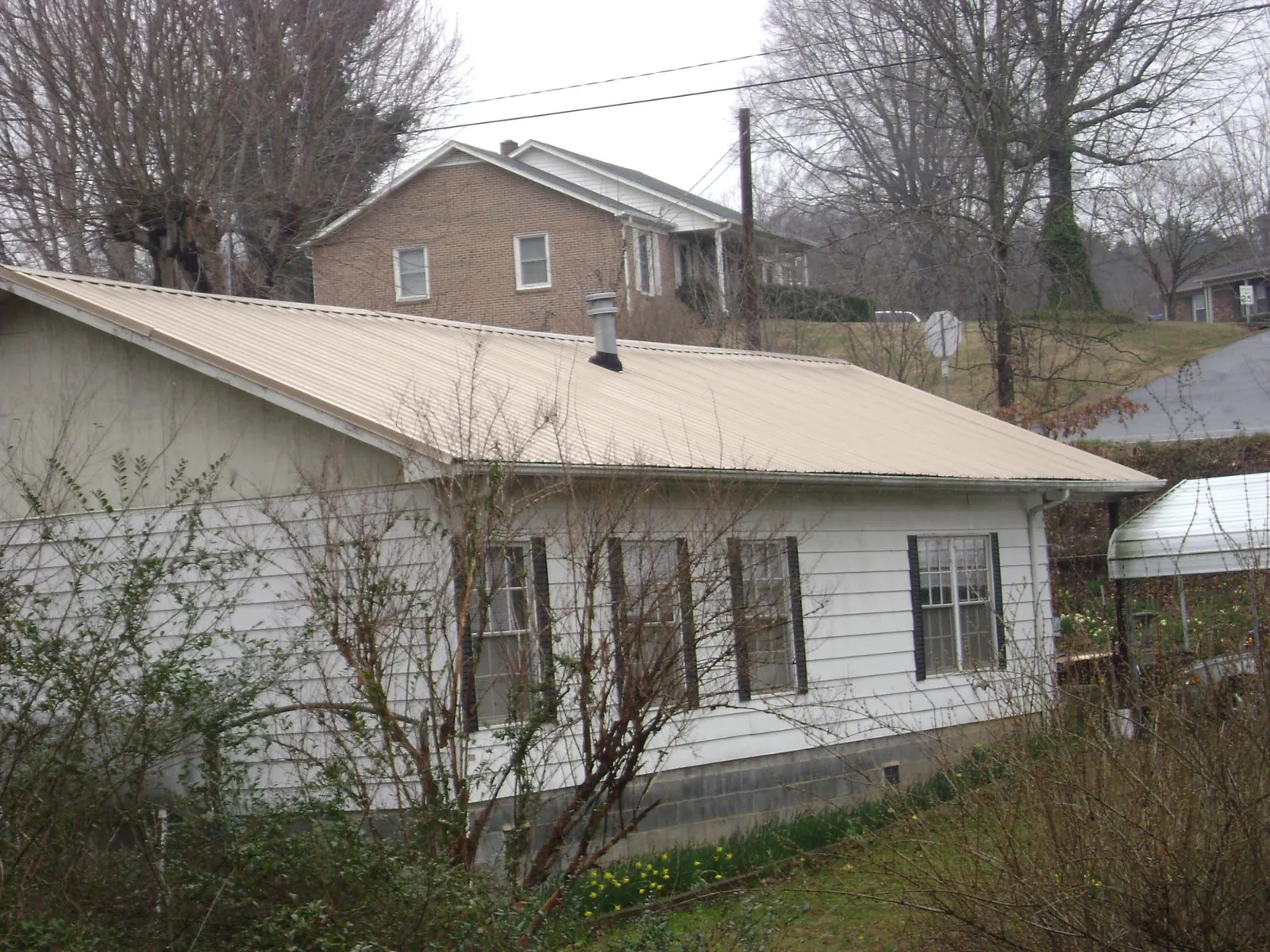 Tan metal roof on a white sided house set into a hillside — Commercial Roofing by Roofing Brothers in Waller