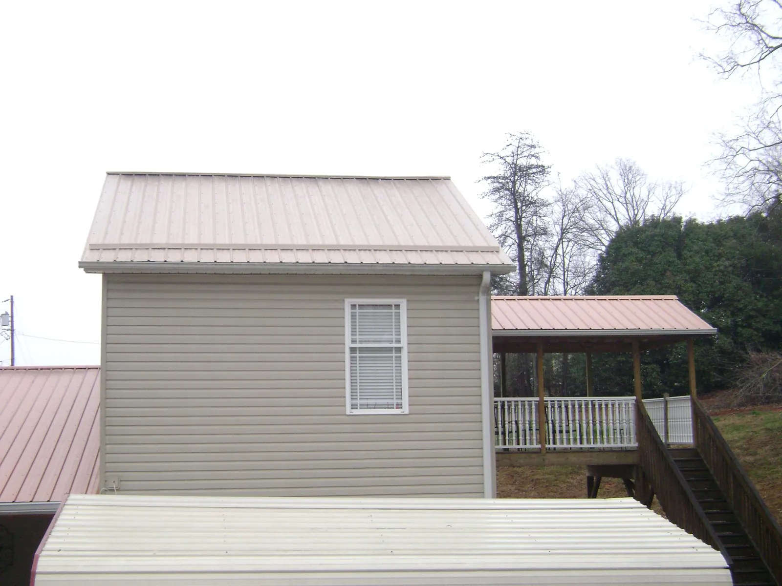 Tan metal roofs on a two story addition and attached porch, from a Roof Replacement job in Waller
